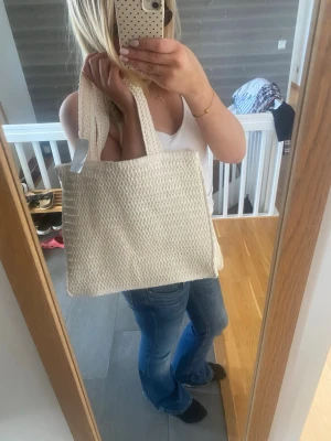 Beige stickad strandväska  - Snygg beige strandväska i stickat material med två breda handtag. Perfekt att slänga över axeln och rymmer allt du behöver till skolan eller stan. Enkel och stilren design som passar till det mesta.