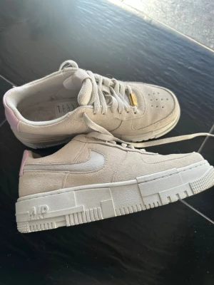 Nike Air Force 1 pixel - Säljer ett par beige Nike Air Force 1 Pixel sneakers i beige mocka med vita detaljer och en hint av ljusrosa på hälen. Aldrig använda, storlek 39. Kvitto + kartong finns. Nypris: 1350kr🩷