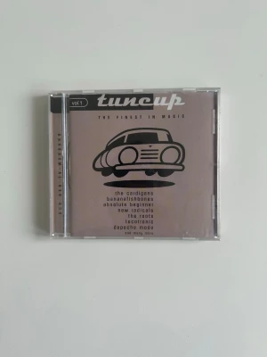 CD Tunecup Vol. 1 The Finest In Music - Tunecup Vol. 1 The Finest In Music är en CD-samling med artister som The Cardigans, New Radicals, The Roots och Depeche Mode. Omslaget är beige med svart tryck och en tecknad bil på framsidan. Plastfodral med tryckt framsida och baksida.