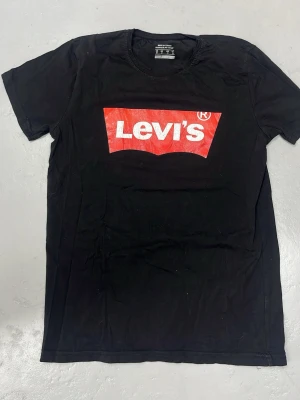 Svart Levi's t-shirt med röd logga - Klassisk svart t-shirt från Levi's med den ikoniska röda loggan tryckt på bröstet. 