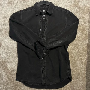 Svart skjorta från G-Star RAW - Säljer en svart långärmad skjorta från G-Star RAW i mjuk bomull. Skjortan har klassisk krage, knappar framtill och en avslappnad passform. Perfekt till jeans o vid köp av fler plagg löser jag rabbat åt dig 🤗