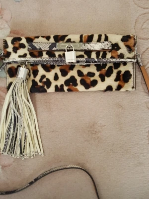 Karen Millen väska med axelrem - Fantastisk fin Karen Millen väska med axelrem, leopardmönstrad. Den är i toppskick oanvänd. Väskan  har dragkedja, toffs och en magnet knapp,  det finns en ficka inuti i väskan.  Mått: längd 25 cm. Hög 17 cm. axelband 100 cm.      Äkta förstås