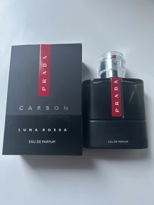 Prada Luna Rossa Carbon EdP 50ml - Prada Luna Rossa Carbon Eau de Parfum i 50 ml flaska. Parfymen kommer i en stilren svart flaska med silverfärgad kork och röd detalj med Prada-logga. Doften är modern och maskulin, perfekt för dig som gillar exklusiva och fräscha parfymer.