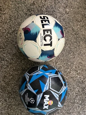 Två handbollar från Select och Max - Två handbollar, en från Select i vitt med blå och lila detaljer, och en från Max i svart med blå och vita mönster. Perfekta för träning eller match. Båda har tydliga loggor och sportig design.