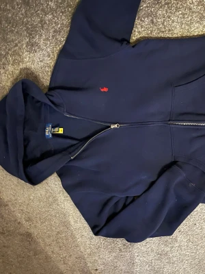 Mörkblå hoodie från Polo Ralph Lauren - Snygg mörkblå hoodie från Polo Ralph Lauren med dragkedja och klassisk röd logga på bröstet. (Är använd enbart en gång)