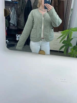 Ljusgrön cardiganjacka - Ljusgrön cardiganjacka med quiltat mönster och stora framfickor. Jackan har rund halsringning, knäppning framtill med knappar och är tillverkad i ett mjukt tyg som ger en avslappnad look. Perfekt för lager-på-lager-stil.