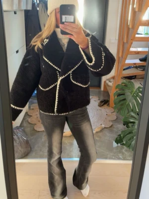 Svart teddyjacka/ kappa med vita detaljer - Säljer en svart teddyjacka med oversized passform och vita kontrastsömmar längs kanterna. Jackan har bred krage och stora fickor framtill. Perfekt för dig som vill ha en mysig och trendig look i vinter.