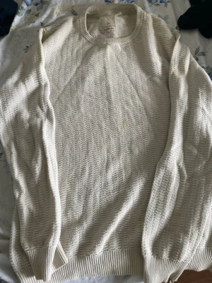 Vit stickad tröja från Homebound - Säljer en vit stickad tröja från Homebound i storlek medium. Tröjan har rund halsringning, ribbade muddar vid ärmslut och nederkant samt ett diskret stickat mönster. Perfekt för lager på lager och enkel att matcha med olika outfits.