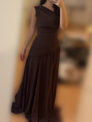Brun långklänning, Babyboo  - Elegant brun långklänning med asymmetrisk axel och draperad överdel. Kjolen är vid och faller snyggt ner mot golvet. Klänningen har en stilren och tidlös design som passar perfekt till speciella tillfällen. Köpt 2 maj för 2118 kr, eftersom returtiden gått ut säljer jag den för 1699 kr.