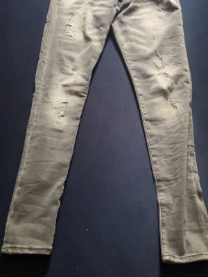 Grå dsquared jeans - Snygga grå dsquared jeans med slitningar på både lår och knän. Jeansen har en tight passform och är perfekta för en avslappnad streetstyle-look. Materialet ser ut att vara en bomullsblandning med lite stretch för extra komfort.