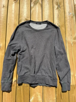 Mörkgrå sweatshirt Tiger of Sweden - En stilren mörkgrå sweatshirt från Tiger of Sweden. Tröjan har rund halsringning, långa ärmar och ribbade muddar vid ärmslut och nederkant. Tillverkad i mjukt bomullsmaterial som känns skönt mot huden. Perfekt för en avslappnad och snygg look.