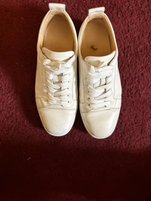 christian Louboutin - Stilrena vita sneakers i skinn med klassisk snörning och platt sula. Skorna har en enkel och tidlös design som passar till det mesta. Perfekta för dig som gillar en clean och minimalistisk look.