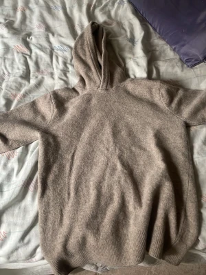 Beige stickad hoodie - Mysig beige stickad hoodie med huva och ribbade muddar. Perfekt för chill dagar och enkel att matcha med jeans eller mjukisbyxor. Materialet känns mjukt och skönt mot huden.