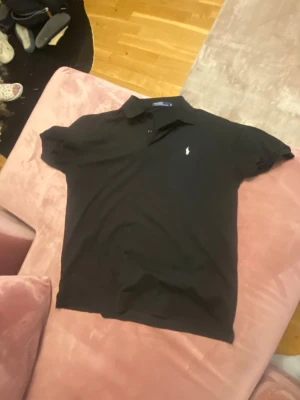 Svart pikétröja från Ralph Lauren - Klassisk svart pikétröja från Ralph Lauren med vit broderad logga på bröstet. Storleken står 3xl men passar mer som L/XL
