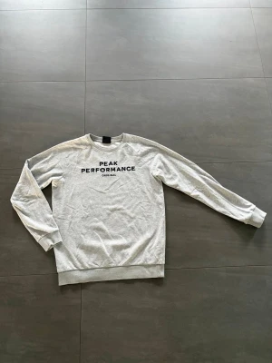 Grå sweatshirt Peak Performance - Ljusgrå sweatshirt från Peak Performance med svart tryck på bröstet.  Väldigt bra skick 