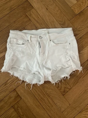 Vita lågmidjade jeansshorts - Säljer ett par vita jeansshorts med fransig kant och råa detaljer. Klassisk femficksmodell med knapp och dragkedja framtill. Perfekta för sommaren💕