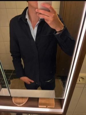 Mörkblå skjorta från H&M Regular Fit - Snygg mörkblå skjorta från H&M i regular fit. Skjortan har klassisk krage, knäppning framtill och långa ärmar. Perfekt för en stilren look och enkel att matcha med jeans eller chinos.