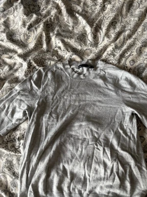 Ljusgrå basic tröja med rund hals - En enkel och stilren ljusgrå tröja med rund halsringning och ribbade muddar. Perfekt för lager-på-lager och passar till det mesta. Tröjan är tunnstickad och har en klassisk passform.