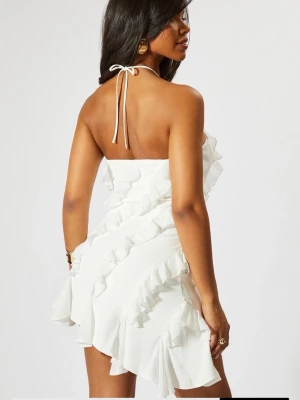 Vit volangklänning med halterneck - Supersnygg vit kort klänning med halterneck och volangdetaljer som går diagonalt över hela klänningen. Klänningen är ärmlös och har en lätt asymmetrisk nederkant. Perfekt för skolavslutning eller studenten!  Säljer denna då den var för stor!