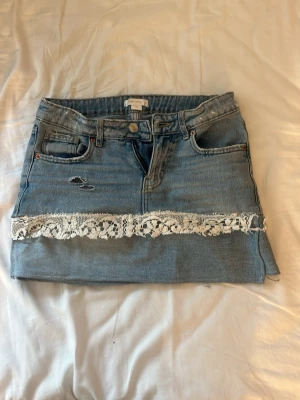 Blå jeanskjol med spets från Gina - Säljer en ljusblå jeanskjol som jag har gjort själv ut av ett par vanliga Gina tricot jeanse med vit spetsdetalj längs nederkanten. Kjolen har klassiska fickor fram och bak, knapp- och dragkedjestängning samt en liten slitning framtill. Perfekt för dig som gillar denim med en söt twist. Den är då för liten för mig tyvärr men hoppas den passa någon annan! Har däremot gått sönder lite på kanterna av spetsen, så om man e sugen så skickar jag bilder på de små detaljerna!