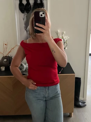 Röd ärmlös topp - Snygg röd topp med bred, något draperad halsringning och ärmlös design. Perfekt att styla med jeans eller kjol för en trendig look. Materialet känns mjukt och stretchigt, vilket gör den bekväm att bära hela dagen.