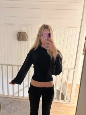Mörkblå croppad stickad tröja - Snygg svart croppad stickad tröja med långa ärmar och hög hals. Tröjan har en figurnära passform och vida ärmar som ger en trendig look. Perfekt att matcha med höga byxor för en stilren outfit.
