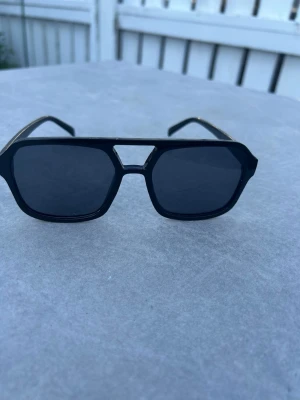 Svarta kantiga solglasögon - Snygga svarta solglasögon med kantig form och bred båge. Glasen är mörka och ramen är i plast med en modern, edgy design. Perfekta för dig som vill sticka ut och addera en cool vibe till din outfit. Väldigt snygga till en dag med strålande sol ☀️ 