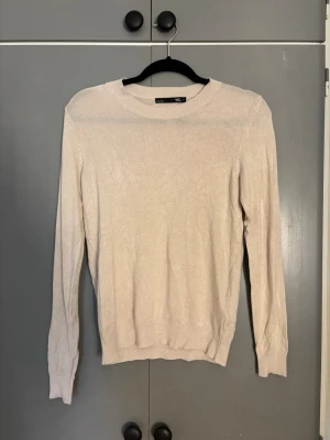 Beige stickad tröja från 157 - Säljer en stilren beige stickad tröja från 157 med rund halsringning och långa ärmar. Tröjan har ribbade muddar vid hals, ärmslut och nederkant. Perfekt basplagg för lager på lager och enkel att matcha med olika outfits.