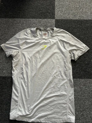 Gymshark T-shirt från 2021 - Säljer min gymshark T-shirt från 2021. Skulle ändå säga att den är i bra skick och svår att få tag i. Den gula gymshark loggan är lite sönder som man kan se på bilden.