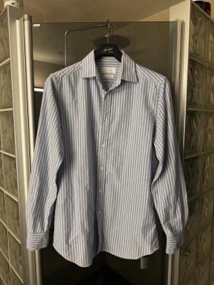 Blåvit randig skjorta - Klassisk blå skjorta med vita ränder från Massimo Dutti. Skjortan har lång ärm, knappar framtill och en stilren krage. Perfekt för en clean och snygg look. .