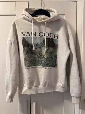 Vit hoodie med Van Gogh-tryck - Säljer en vit hoodie från Pull&Bear med ett stort Van Gogh-tryck på bröstet och texten 'Mademoiselle Gachet in the Garden'. Hoodien har dragsko i huvan och ribbade muddar vid ärmslut och nederkant. Perfekt för dig som gillar konst och streetwear.