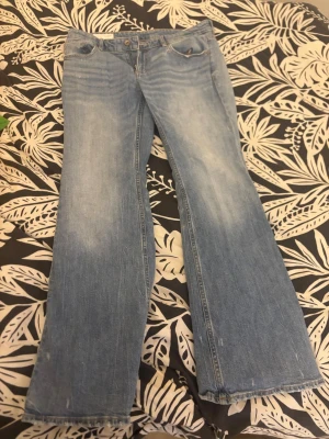 Ljusblå bootcut jeans - Säljer ett par ljusblå bootcut jeans med klassisk femficksdesign och lätt slitna detaljer. Jeansen har utsvängda ben och är tillverkade i denim med en skön vintagekänsla. Perfekta för dig som gillar retrostil och vill ha ett par bekväma jeans med snygg passform.