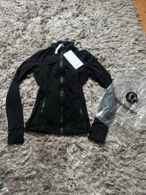  Lululemon jacka  - Snygg svart träningsjacka från Lululemon med figurnära passform, hel dragkedja framtill och två dragkedjeförsedda fickor. Tillverkad i stretchigt funktionsmaterial som andas. Perfekt för gymmet eller löprundan.