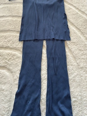 Mörkblå ribbat set med vida ben - Säljer ett mörkblått ribbat set med lång överdel och matchande byxor med utsvängda ben. Setet har en mjuk och stretchig känsla, perfekt för en avslappnad look. Materialet är troligtvis bomullsblandning. Inga synliga märkesloggor.