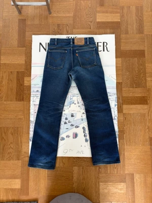 Levi's blå bootcut jeans - Säljer ett par gjorda i Italien blå Levi's orange tabs  jeans med bootcut passform. Jeansen har fem fickor, kontrastsömmar och en läderpatch bak i midjan. Materialet är kraftig denim i bomull och färgen är mörkblå med lätt slitning på knän och lår. Gjorde på 90talet