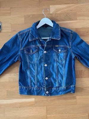 Mörkblå jeansjacka från Diesel  - Klassisk mörkblå jeansjacka från Diesel med silverfärgade knappar och två bröstfickor med lock. Storlek M. Snygga sömmar och tidlös design som passar till det mesta. Jackan har en rak passform och typisk jeansjackekrage.