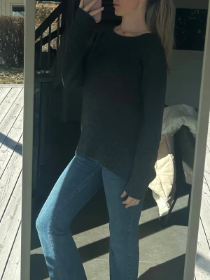 Stickad tröja  - En enkel och stilren mörkgrå stickad tröja med rund hals och långa ärmar. Tröjan har ribbade muddar vid ärmslut och nederkant samt en avslappnad passform. Perfekt att bära till jeans eller kjol. 