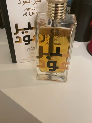 Ameer Al Oudh Intense Oud parfym - Ameer Al Oudh Intense Oud från Lattafa är en parfym i en elegant, rektangulär glasflaska med guldfärgad vätska och guldfärgad kork. Flaskan har svart och guld text på framsidan och rymmer 100 ml Eau de Parfum. Doften har orientaliska och träiga toner.  Ungefär 80% kvar