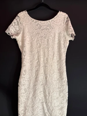 Vit spetsklänning med v-ringning - Superfin vit kortklänning i spets med blommigt mönster och korta ärmar. Klänningen har en snygg v-ringning i ryggen och är fodrad undertill. Perfekt för sommarens alla tillfällen och ger en romantisk vibe. Perfekt till student