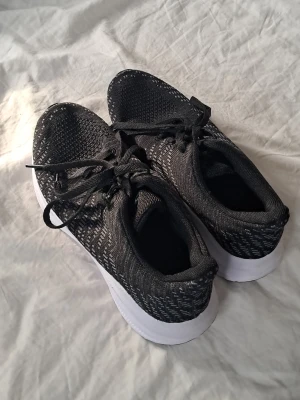 Svarta sneakers med vit sula - Snygga svarta sneakers med stickad mesh-överdel och vita sulor. Skorna har svarta skosnören och en låg profil som ger en sportig look. Perfekta för dig som gillar stilrena och bekväma skor till vardags.