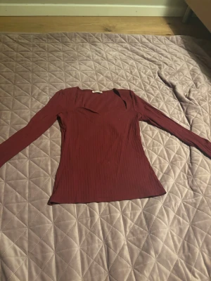 Vinröd ribbad långärmad topp - Snygg vinröd långärmad topp med ribbad struktur och v-ringning. Figurnära passform som framhäver siluetten. Perfekt att styla med jeans eller kjol för en trendig look. 