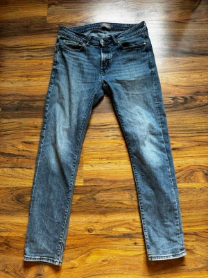 Blå slim fit jeans  - Säljer ett par blå slim fit jeans med lätt slitna detaljer och klassisk femficksdesign. Jeansen har normal midja och raka ben. Materialet är denim i bomull med en snygg tvättad look. Perfekta för en avslappnad och trendig stil. 