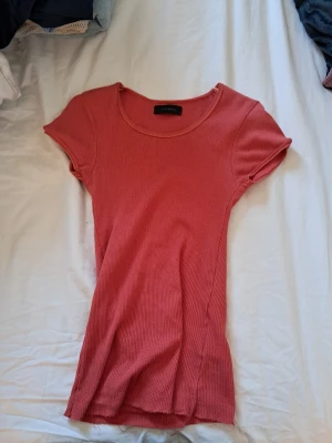 Ribbad rosa topp från Vero Moda - Supersnygg ribbad topp i rosa från Vero Moda. Modellen har rund halsringning och korta ärmar, perfekt till jeans eller kjol. Materialet är mjukt och stretchigt för en bekväm passform. Enkel men trendig design som är lätt att matcha.