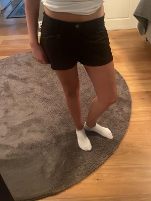 Svarta shorts med dragkedjor - Snygga svarta shorts med dragkedjor framtill. De har en midwaist passform och är perfekta för sommaren. Stilen är enkel och modern, vilket gör dem lätta att matcha med olika toppar.