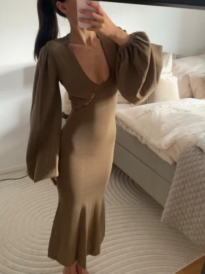  långärmad maxiklänning - Säljer en snygg maxiklänning med djup v-ringning och vida armar från adoore. Klänningen har figurnära passform och dekorativa knappar framtill. 