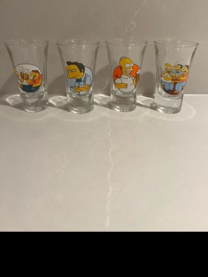 The Simpsons shotglas 4-pack - Fyra shotglas i genomskinligt glas med färgglada motiv från The Simpsons. Varje glas har olika karaktärer från serien tryckta på framsidan, bland annat Homer och Moe. Perfekt för samlare eller som rolig detalj till festen.