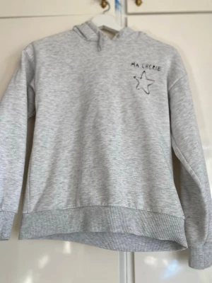 Grå hoodie med tryck 'Ma Chérie' - Ljusgrå hoodie med huva och svart tryck på🤍 mental detaljerna som ska sitta längs ut på snörena är borta.