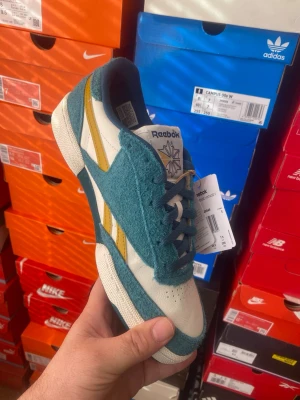 Reebok Club C  - Snygga Reebok sneakers med blå mockadetaljer, vita partier i läder och gula ränder på sidan. Skorna har klassisk låg profil, perforerad tå och Reebok-logga på plösen. Perfekta för dig som vill ha en retrovibe i din stil.