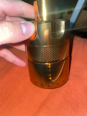 Azzaro forever Wanted elixir - Azzaro Wanted parfym i en cool, cylinderformad flaska med metallisk guldfinish. Flaskan har ett greppvänligt mönster i mitten och en robust, modern design som sticker ut på hyllan. Perfekt för dig som gillar exklusiva och snygga parfymflaskor. 100ml