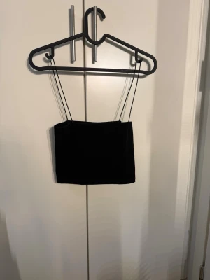 Svart ärmlös linnetopp - Minimalistisk svart linnetopp med tunna axelband och rak skärning. Perfekt att styla med jeans eller kjol för en clean look. Tidlös och enkel design som passar till många outfits.